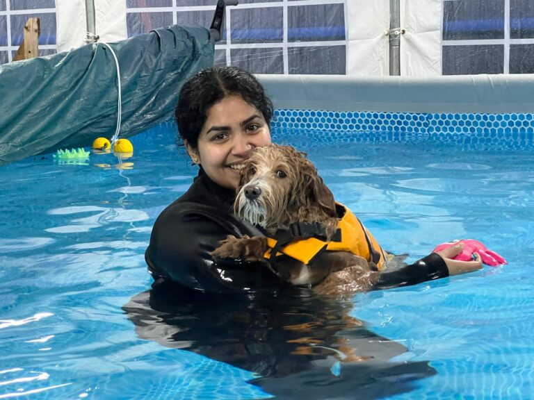 Owner swimming alongside their dog in the heated indoor pool